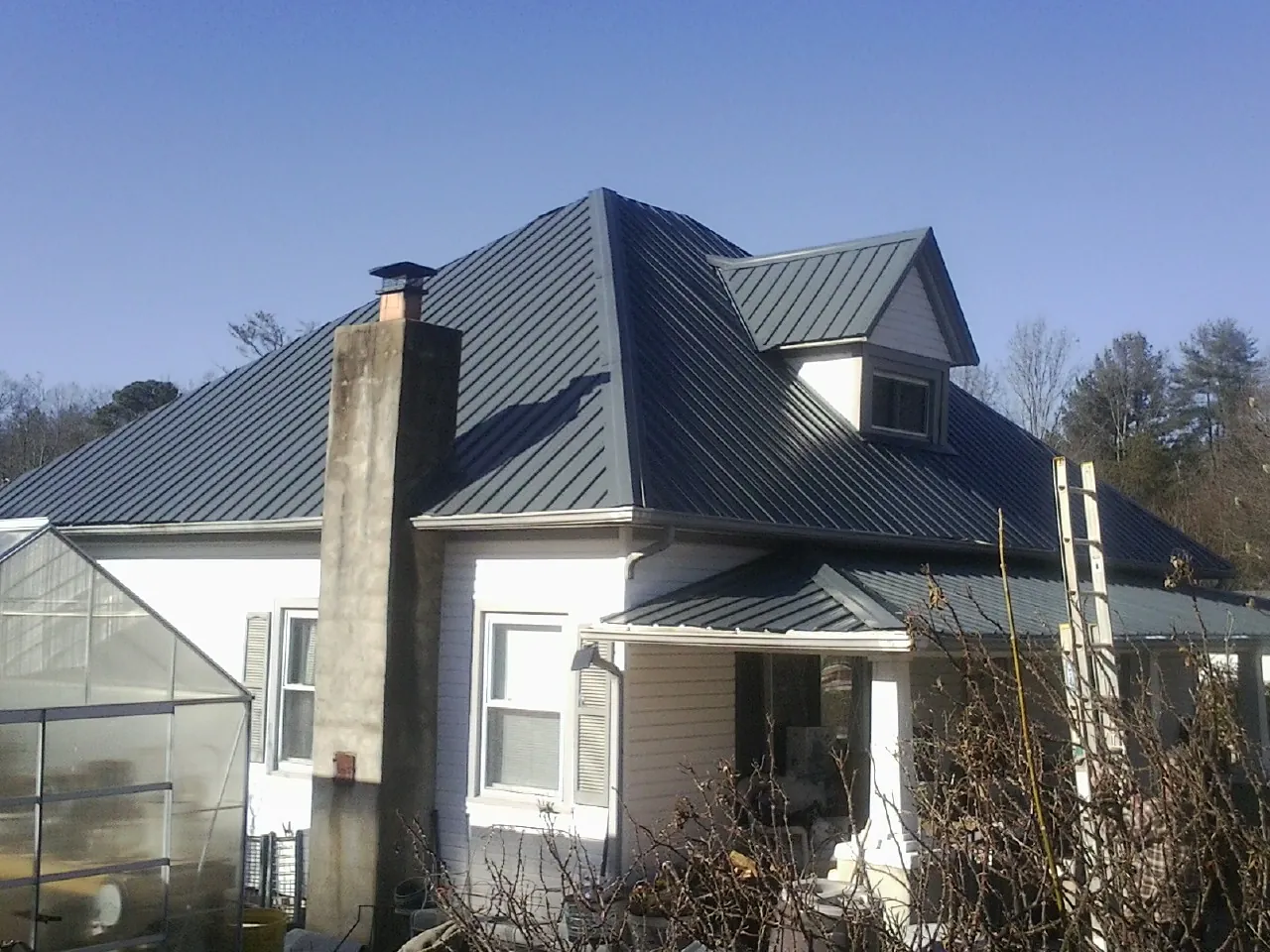 Dark blue standing seam metal roof on a white farmhouse with dormer — Slate & Tile Roof Repair by Roofing Brothers in Ridgecrest
