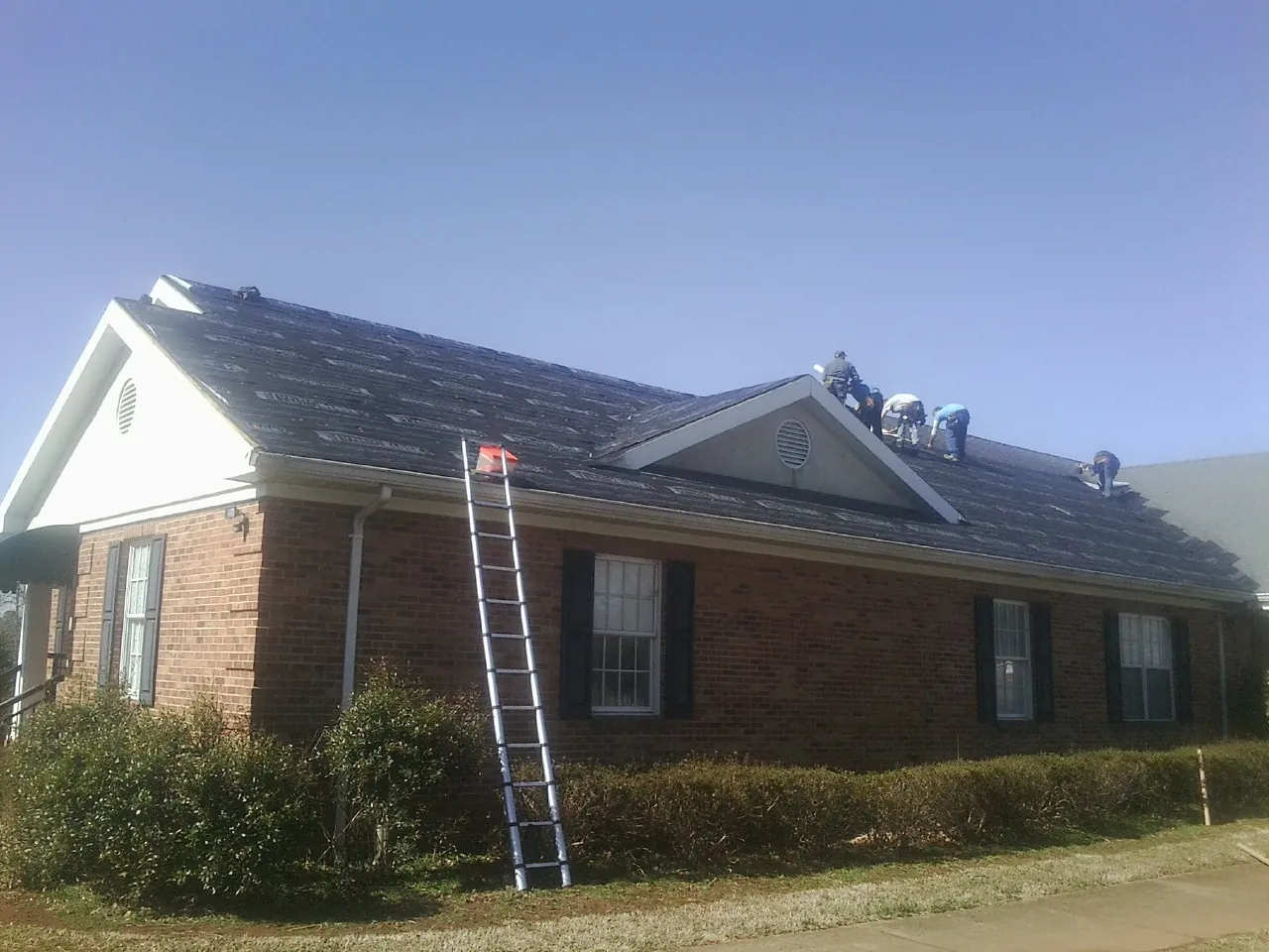Crew tearing shingles off a brick ranch roof with a ladder set — Emergency Roof Repair work by our crew in Ridgecrest