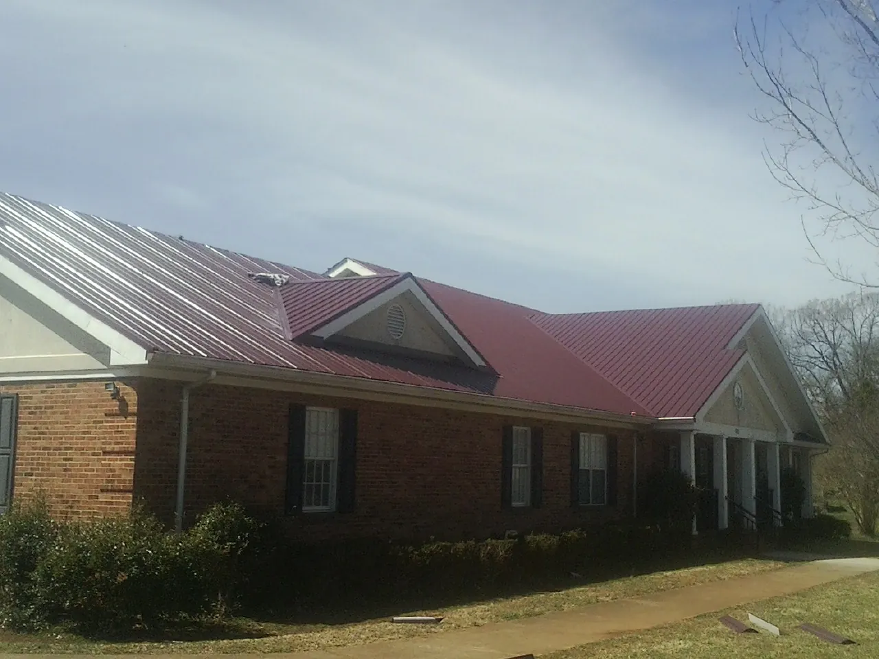 Red metal roof with gabled entries on a long brick building, from a Hail Damage Roof Repair job in Ridgecrest