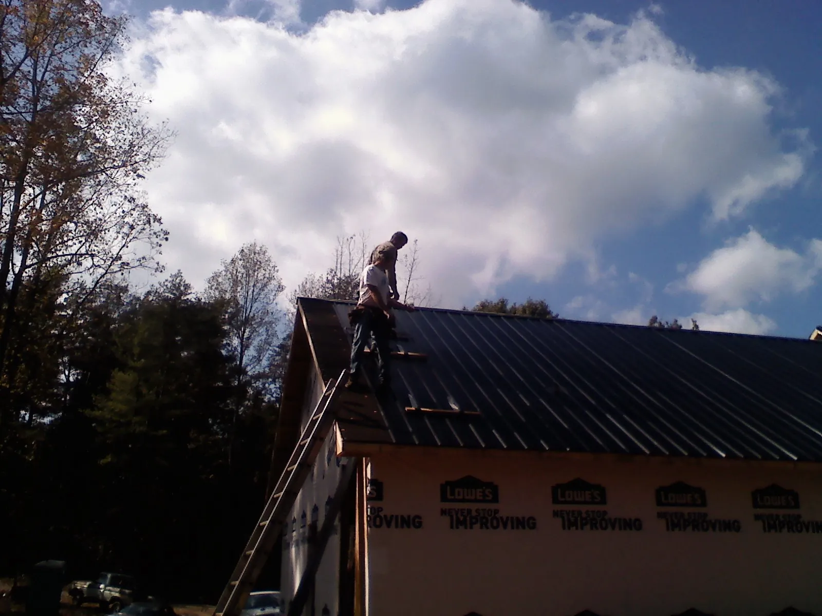 Roofer fastening dark metal panels high against a cloudy sky, from a Roof Inspection job in Ridgecrest