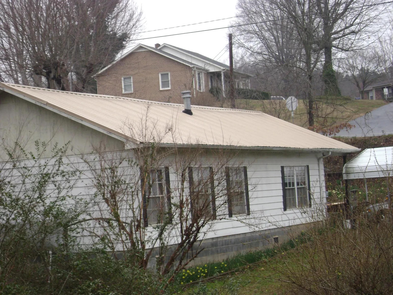 Tan metal roof on a white sided house set into a hillside — Commercial Roofing by Roofing Brothers in Ridgecrest